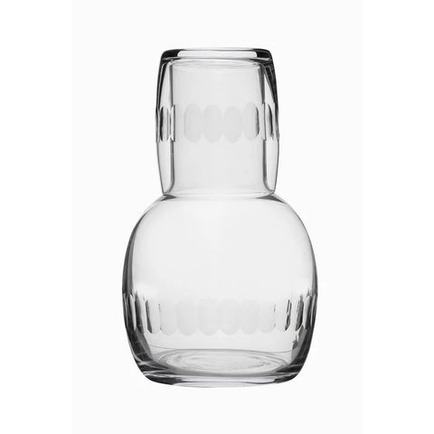 A glass carafe with a lens design with a matching glass cup upside down at its mouth. 