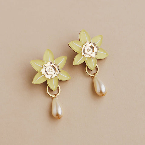 A pair of yellow acrylic daffodil shaped earrings with a pearl hanging from each against a pink background.