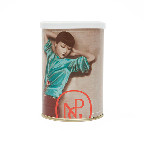 Round coffee can featuring a photograph of Anna May Wong lying down in a blue velvet top, with the NPG logo below in red. 