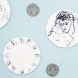 Two white plates with blue ink drawings are displayed alongside two round marbled coasters in blue and green.