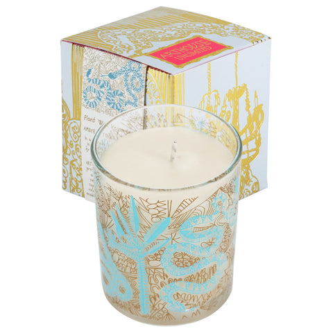 Glass candle with gold abstract design and bright blue snakes and trees on the outside.