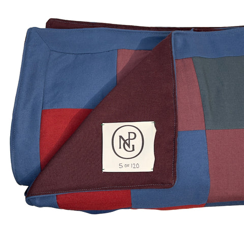 Close up detail of the neatly folded red and blue chequered throw blanket with the top layer folded down, exposing the NPG logo.