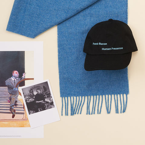 A collection of Francis Bacon products including a blue scarf, black Francis Bacon: Human Presence hat, mini print of man walking down stairs and a black and white postcard photograph of Francis Bacon.