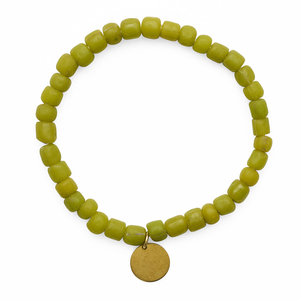 Green beaded bracelet with a circular brass metal charm on a white background