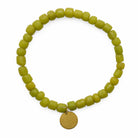 Green beaded bracelet with a circular brass metal charm on a white background