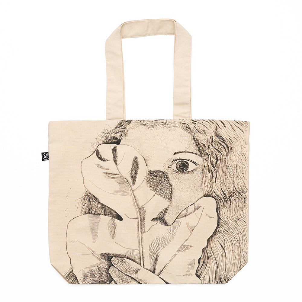 Tote bag with an illustration of a face and leaves on a beige canvas material.