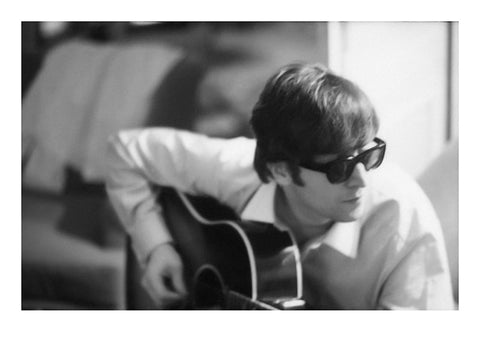 Black and white photograph of John Lennon wearing sunglasses and playing guitar, taken by Paul McCartney.