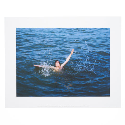 Photographic mini print featuring John Lennon swimming in the sea and splashing water, taken by Paul McCartney.