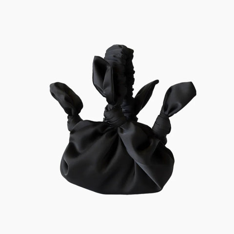 A round black satin bag with knot details and a scrunchie style handle.
