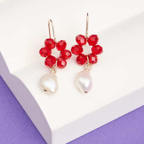 Dangling earrings with red glass beads in a flower shape with pearls hanging from the bottom.