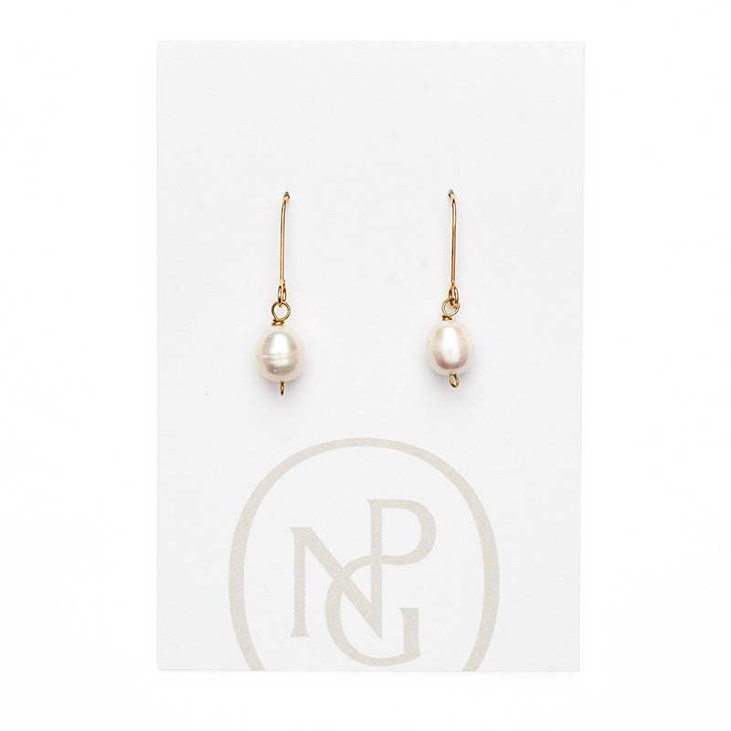 A pair of earrings featuring a single pearl hanging form a gold hook attached to npg packaging.