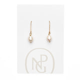 A pair of earrings featuring a single pearl hanging form a gold hook attached to NPG packaging.