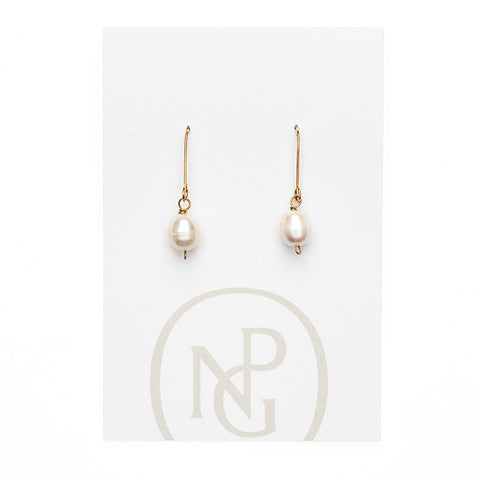 A pair of earrings featuring a single pearl hanging form a gold hook attached to NPG packaging.