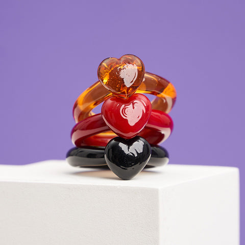 A set of 3 heart shapes glass rings in amber, red and black stacked on top of each other.
