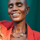 Woman in red jacket wearing a gold chunky necklace and gold loop earrings. 