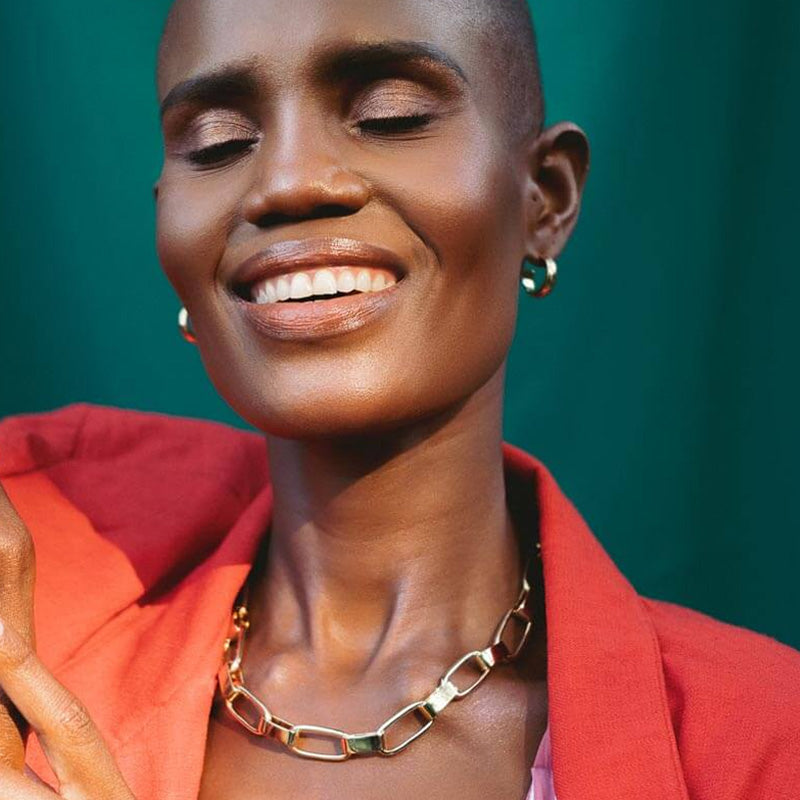 Woman in red jacket wearing a gold chunky necklace and gold loop earrings. 