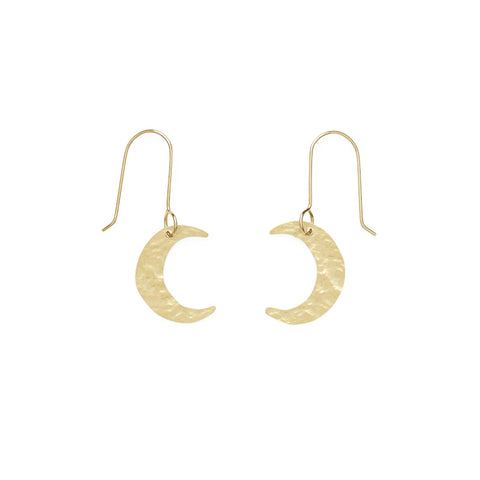 A pair of small hammered brass moon pendants hang from gold earrings hooks.