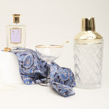 A blue paisley coloured pocket square draped around cocktail glasses and perfume.