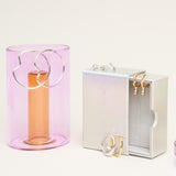 A collection of gold and silver jewellery on jewellery boxes and pastel coloured vases.