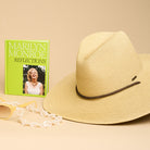 A straw hat and green book titled 'Marilyn Monroe Reflections' against a beige background.