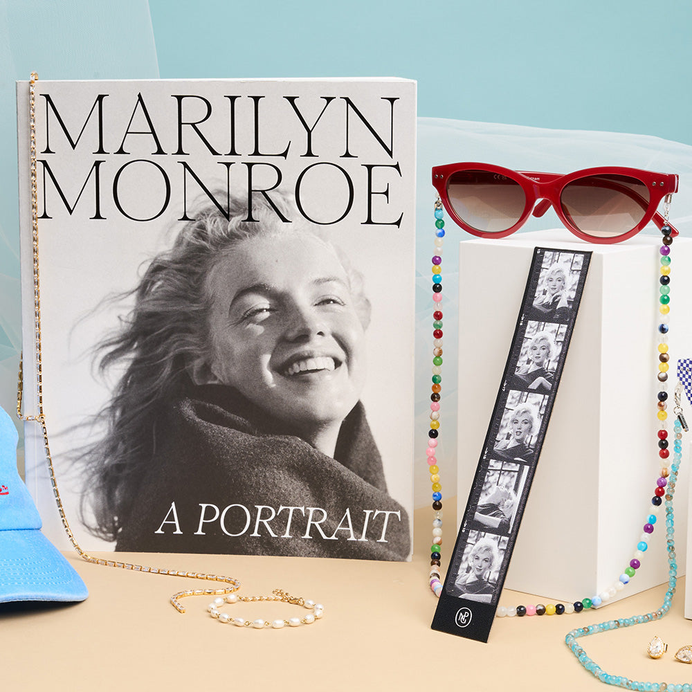 Book titled 'marilyn monroe: a portrait' with sunglasses and a necklace on a light blue background