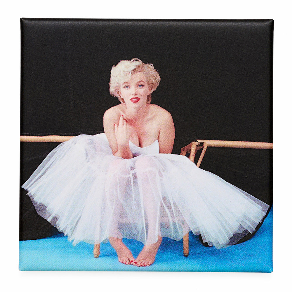 Fridge magnet with a vintage style image of a woman in a white dress sitting on a blue platform.