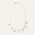 A delicate gold chain necklace featuring seven teardrop-shaped pale pink gemstone pendants and small pearl-like beads, displayed on a clean off-white background.