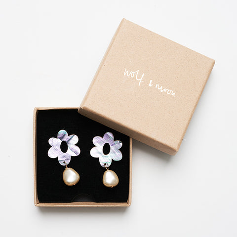 Iridescent flower studs with a dangling pearl in its Wolf & Moon packaging
