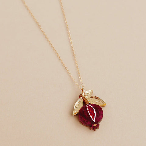 A small acrylic pomegranate pendant in red and gold hanging from a gold chain.