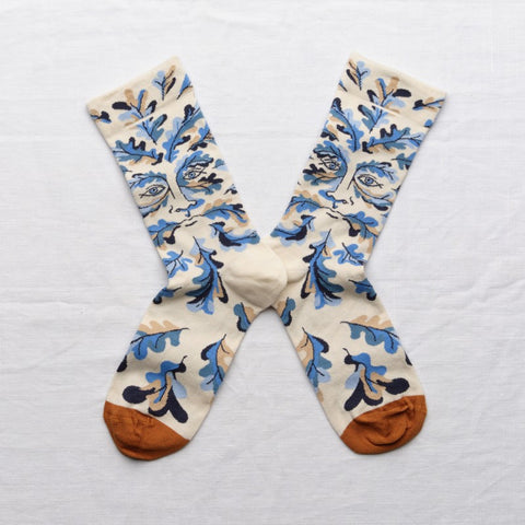 Off-white socks featuring blue, black and beige leaves and a face with terracotta toes.