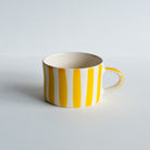Wide ceramic mug with handle and painted yellow vertical stripes. 