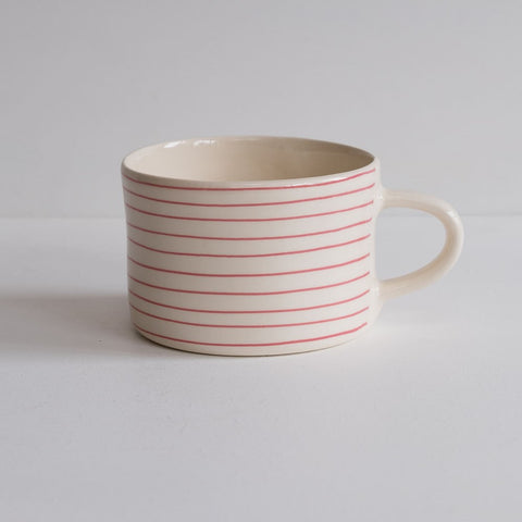 A low wide mug featuring thin painted rose pink stripes.