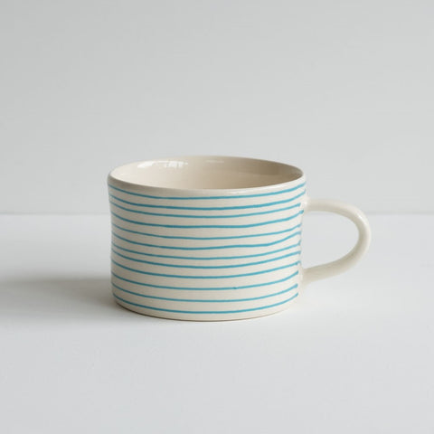 A low wide mug featuring thin painted turquoise stripes.