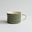 A single mug with a handle and a scratched white stripe design against deep green.