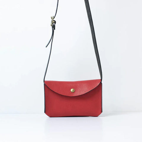 Small rectangular leather bag in red with contrasting black strap and gold popper closure.