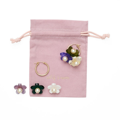 Disassembled hoop earring and flower charms against a pink drawstring bag.