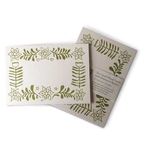 A blank white card with green ferns and flowers bordering the card. 