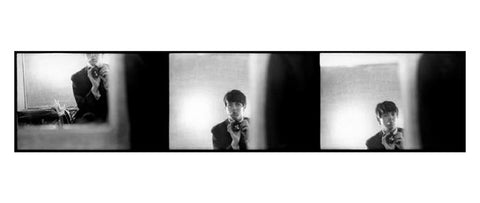 Black and white photographic long postcard featuring three self-portraits of Paul McCartney holding a camera in a mirror reflection.