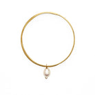 Gold bangle bracelet with a single hanging pearl pendant. 