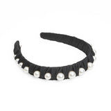 A black headband with fabric ruffles and multiple large round pearls.