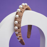 A brown headband with fabric ruffles and large pearls balances on a white arch.