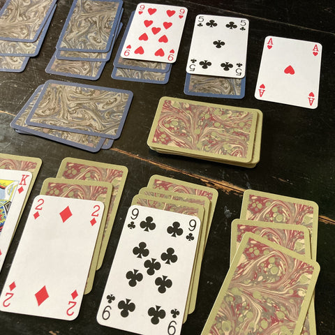 Two deck of cards, showing their front and backs, with the numbers and suits on one side and the marbled design on the back.