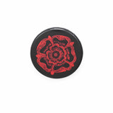 A round black badge with a red illustration of a Tudor Rose.