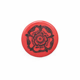 A small badge with a red background and a black Tudor rose emblem on it.