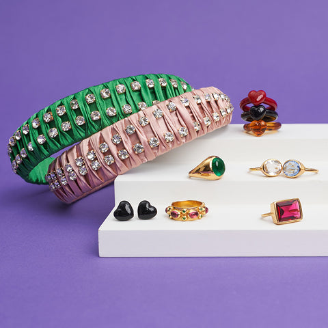 Styled shot of several rings, including our gold one with the green stone, on small steps with one green headband and one pink headband. 