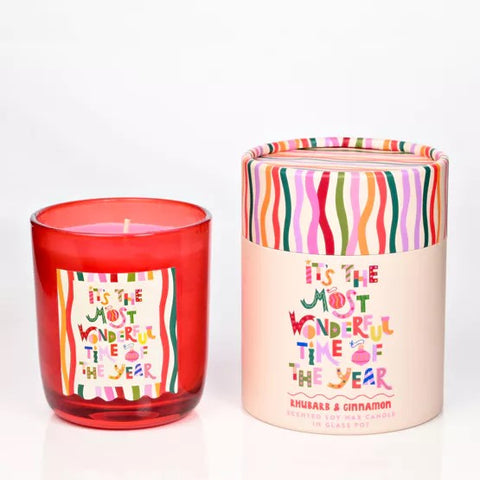 A red glass candle and its cylindrical white and colourful packaging. 