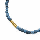 Close up of necklace with round blue beads and a gold cylindrical accent on a white background
