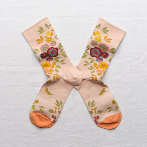 A pair of peach colour socks with pink roses and yellow peonies and an orange toe.