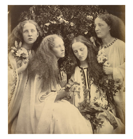 Photographic postcard of four young women in a garden holding flowers. 