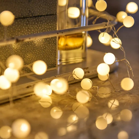 A set of fairy lights on a wire with round white LED light balls on a wooden table against a white metal container.